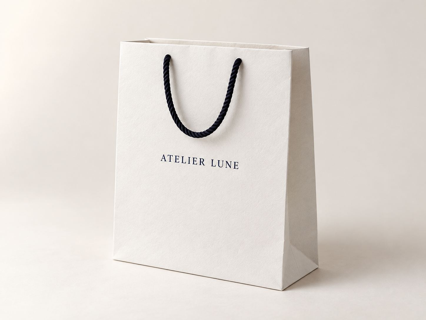 White kraft shopping bag with a short black cotton rope handle and a navy example wordmark.